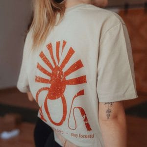Rückenansicht des beigen youyoga Shirts mit dem großen, rostroten Sonnen-Symbol und dem Slogan „breathe deep • stay focused“.