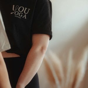 Seitenansicht einer Frau im schwarzen youyoga Community Shirt mit dem markanten Logo-Aufdruck auf der Brust.