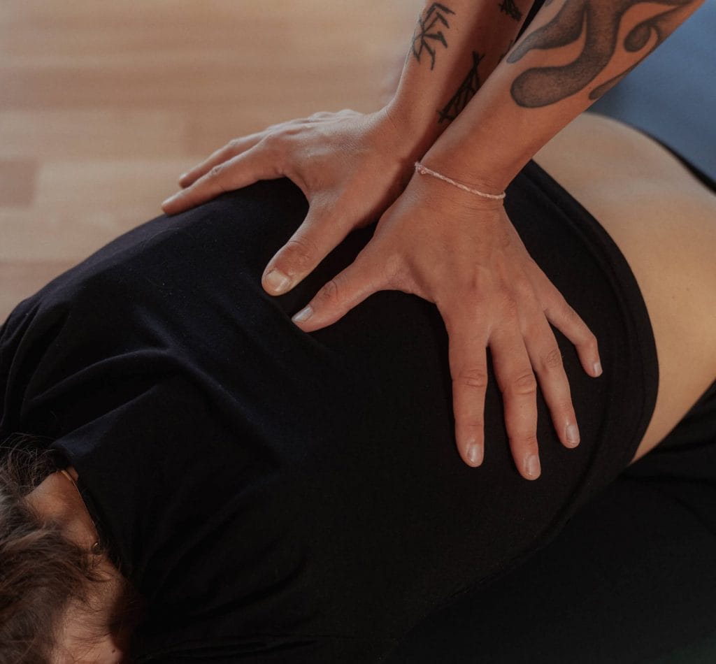 Wohltuendes Adjustment im Yin & Yang Yoga bei youyoga Rostock: Hände geben sanften Druck auf den unteren Rücken zur Vertiefung der Entspannung und Erdung.