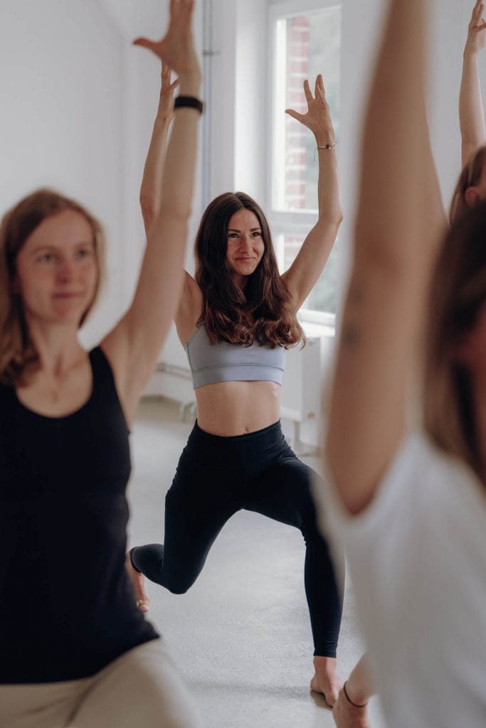 Teilnehmerinnen in einer fokussierten Ausfallschritt-Variation (Anjaneyasana) während des Sonnengruß Tutorials im youyoga Studio Rostock.