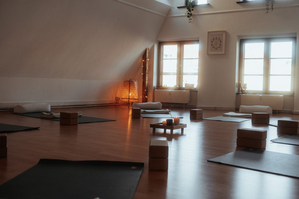 Einladender Wohlfühlort bei youyoga Rostock: Der lichtdurchflutete Übungsraum mit ausgelegten Matten, Hilfsmitteln und stimmungsvoller Beleuchtung.