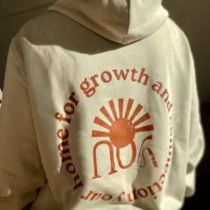 Alternativer Text (Alt-Text): Detailansicht des kreisförmigen Rückenaufdrucks „your home for growth and connection“ auf dem beigen youyoga Community Hoodie