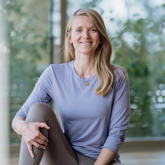Porträt von Yogalehrerin Sylva Bolduan in entspannter Sitzhaltung im lichtdurchfluteten Studio